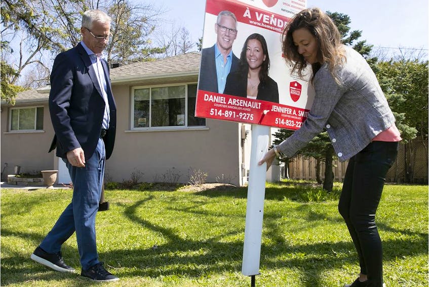 The husband and wife real estate team of Dan Arsenault and Jennifer Smith of of Royal Lepage Village in Pointe-Claire place a for-sale sign on a front lawn on May 14, 2020.