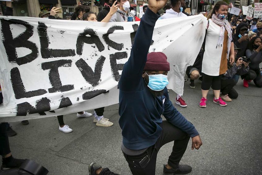 A protester raises his fist and puts a knee to the ground during an anti-racism and anti-police brutality demonstration in Montreal on Sunday May 31, 2020.