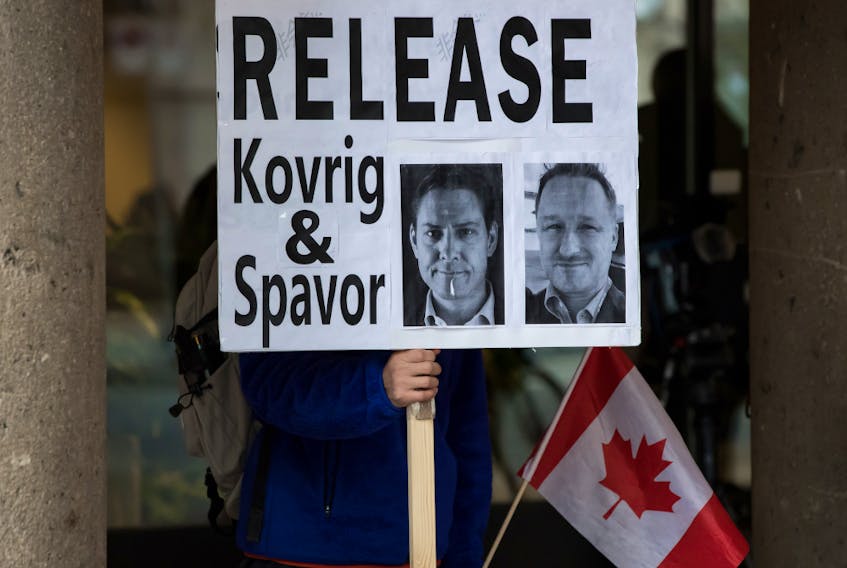 A young man holds a sign bearing photographs of Michael Kovrig and Michael Spavor, who have been detained in China for more than a year, outside the B.C. Supreme Court, where Huawei chief financial officer Meng Wanzhou was attending a hearing, in Vancouver, on Jan. 21.
