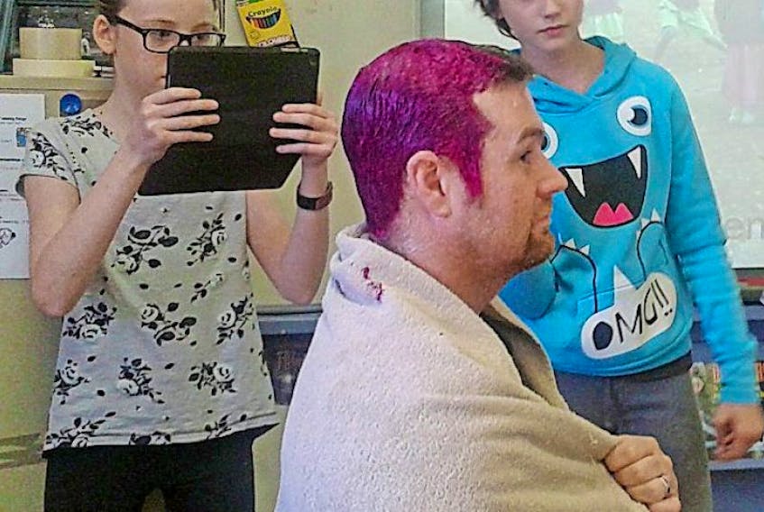 Morell Consolidated School students Christina O'Hanley, left, and Angelica Garcia watch as Grade 7 teacher Desi Doyle gets his hair dyed.