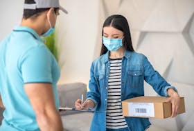 A woman signs for a package while wearing personal protective equipment.