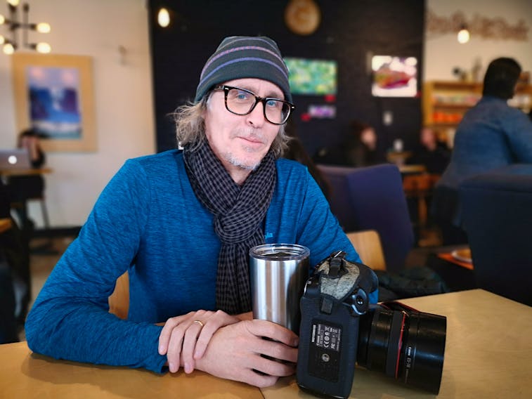 David Howells sitting in his office — a coffee shop — with his YETI mug named Greta and a camera he would never sell. Andrew Waterman/The Telegram