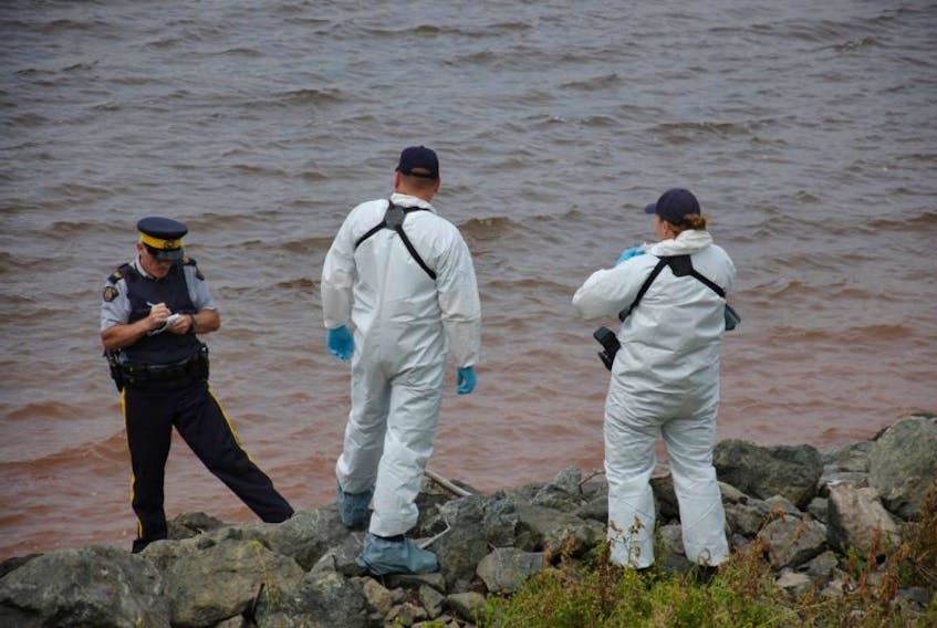 An RCMP officer takes notes as forensic officers look on at the scene where a body has washed up on the rocks near the Hillsborough Bridge.