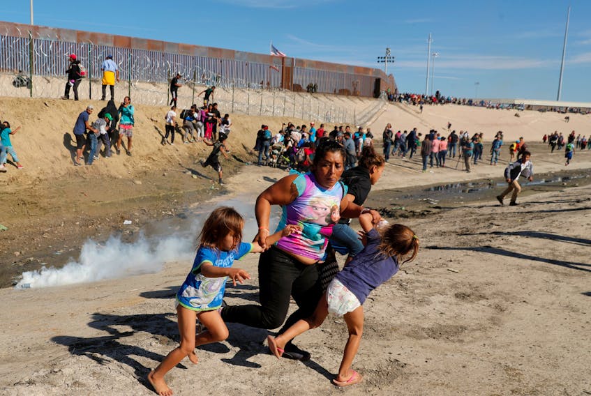 Maria Lila Meza Castro, a 39-year-old migrant woman from Honduras, part of a caravan of thousands from Central America trying to reach the United States, runs away from tear gas with her five-year-old twin daughters Saira Nalleli Mejia Meza, left, and Cheili Nalleli Mejia Meza in front of the border wall between the U.S. and Mexico, in Tijuana, Mexico, Nov. 25, 2018. Kim Kyung-Hoon / Reuters