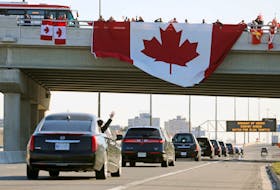 A man waves from a convoy of hearses after a repatriation ceremony for six Canadian military personnel killed in a helicopter crash in the Mediterranean, as they pass under a large Maple Leaf flag hanging from an overpass on the Highway 401 in Toronto, Ont,, on Wednesday, May 6, 2020.
