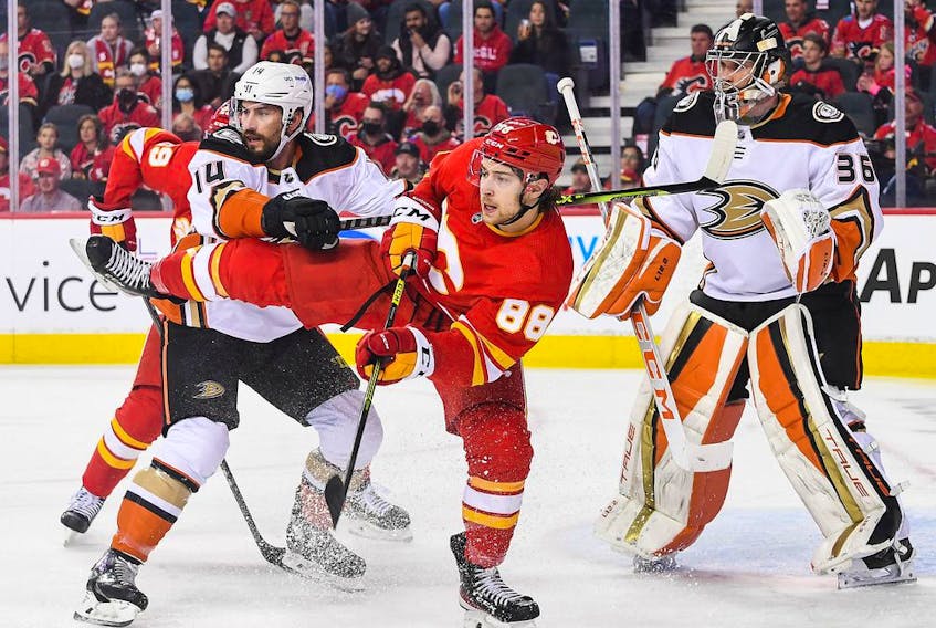  The Anaheim Ducks’ Adam Henrique shoves the Calgary Flames’ Andrew Mangiapane in front of Ducks goaltender John Gibson at the Scotiabank Saddledome in Calgary on Monday, Oct. 18, 2021.