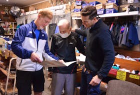 P.E.I. runners Francis Fagan, left, and Stan Chaisson, right, hand an 80th birthday card to long-time runner and sneaker salesman Salam Hashem on Oct. 22.