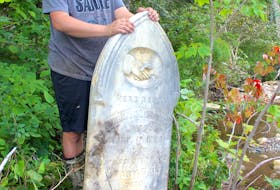 Jeffrey Parks, a 26-year-old antique dealer from Middle River, stands beside a headstone he lifted after it had fallen down an eroding embankment into the Baddeck River this spring. “I hate the idea of being forgotten and this is terrifying to me. I don’t want to end up like this,” he said. CHRIS CONNORS/CAPE BRETON POST