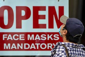 A pedestrian wearing a mask reads signage stating “Open Face Masks Mandatory” in Toronto during the pandemic.
