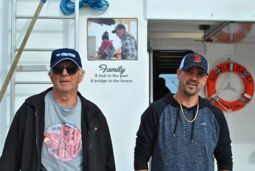 Woods Harbour fishermen Davis and Jeremy Nickerson stand by a photo of  Jeremy when he was three and his grandfather Merle that is on the back of the wheelhouse of the Nuzzle Loader. The father and son are the third and fourth generation LFA 34 commercial lobster fishermen.  KATHY JOHNSON