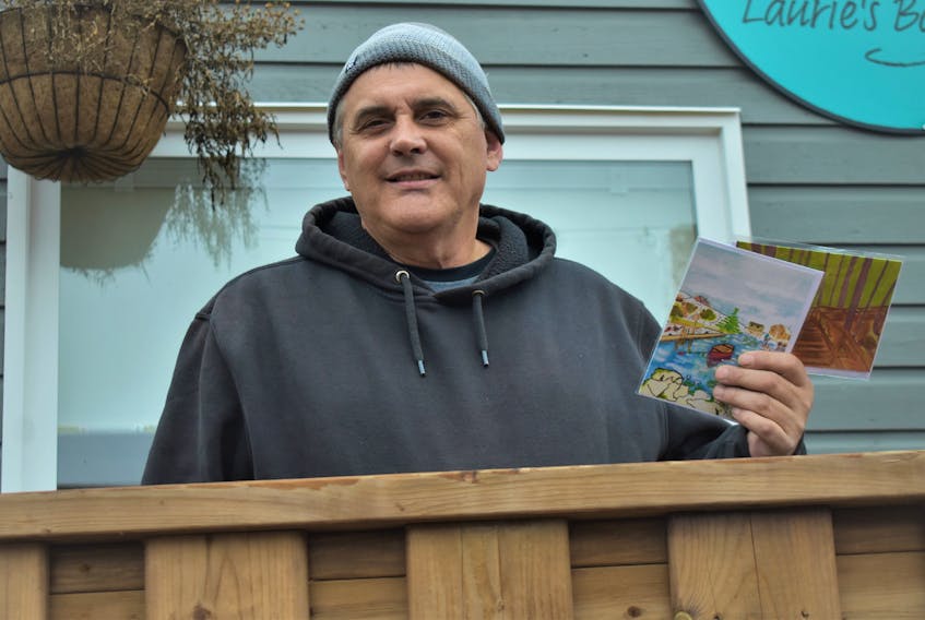Pictured just outside of a Tatamagouche Main Street business, artist Ron McCormick holds up a couple of the cards that are being given away as part of his Cards of Comfort initiative.