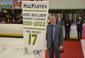 Donnie MacFadyen poses with a banner that now hangs at MacLauchlan Arena recognizing the Charlottetown resident’s 21 years of involvement with the UPEI women’s hockey program. In the background are Panthers head coach Bruce Donaldson, right, and MacFadyen’s parents, Gerald and Joyce MacFadyen. 