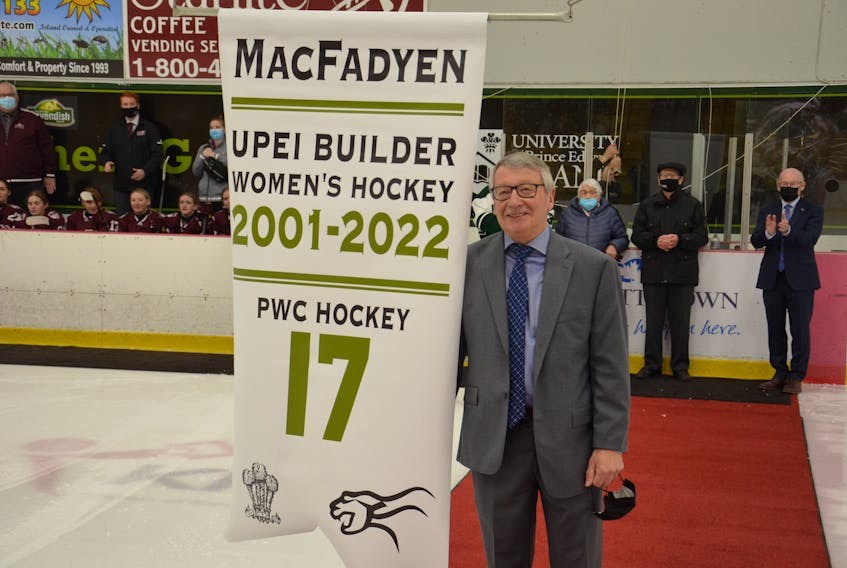 Donnie MacFadyen poses with a banner that now hangs at MacLauchlan Arena recognizing the Charlottetown resident’s 21 years of involvement with the UPEI women’s hockey program. In the background are Panthers head coach Bruce Donaldson, right, and MacFadyen’s parents, Gerald and Joyce MacFadyen. 