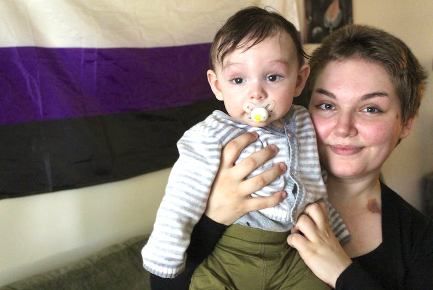 Rinn Carriere holds their five-month-old son John-Kingston Carriere inside their Sydney home on Nov. 1. Behind them hangs the nonbinary flag, which Carriere identifies as her gender. NICOLE SULLIVAN/CAPE BRETON POST 
