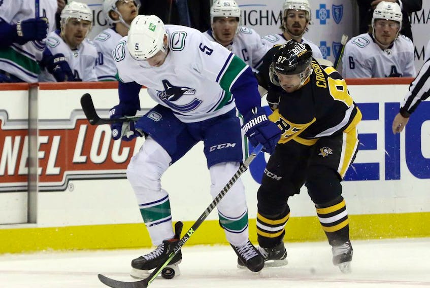 Vancouver Canucks defenceman Tucker Poolman and Pittsburgh Penguins captain Sidney Crosby fight to control the puck on Nov. 24, 2021.
