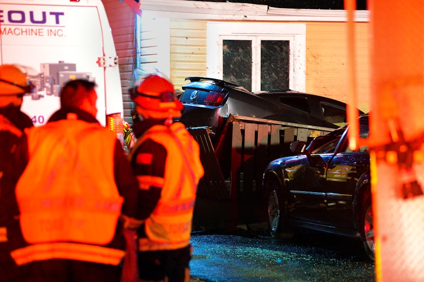 Firefighters check on a car that crashed into two vehicles and a house after it went airborne during a crash Sunday night in Torbay. Keith Gosse/The Telegram