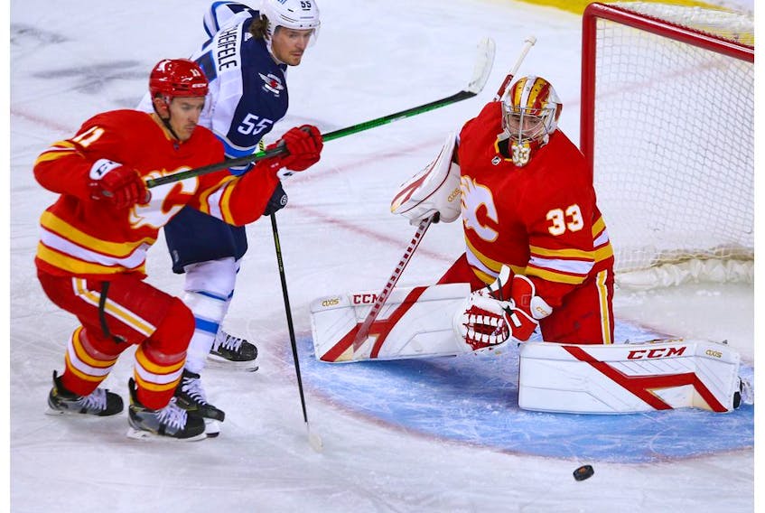 Calgary Flames goaltender David Rittich keeps his eyes on a puck with the Winnipeg Jets’ Mark Scheifele and the Flames’ Mikael Backlund at the Saddledome in Calgary on Saturday, March 27, 2021. 