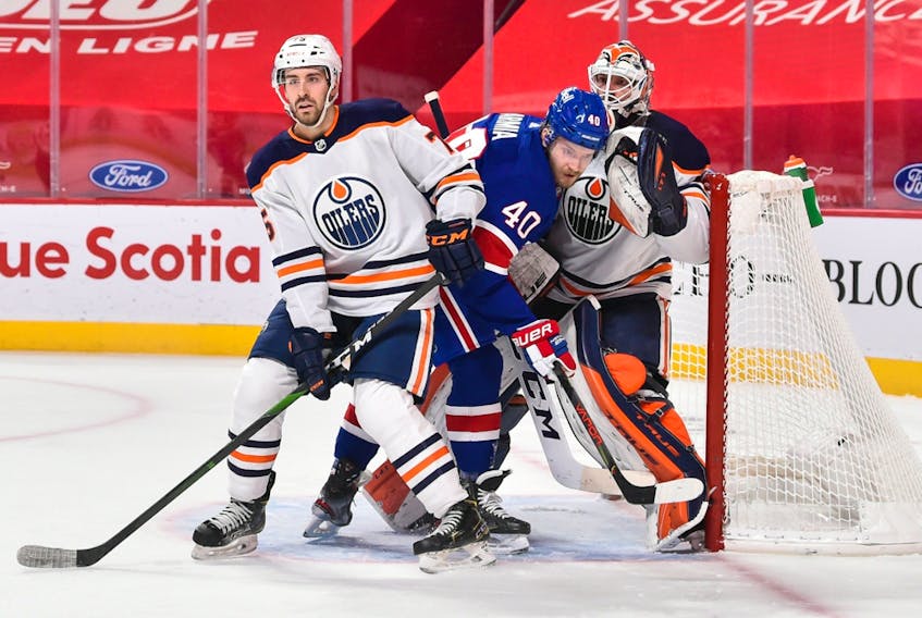 Evan Bouchard (75) of the Edmonton Oilers and Joel Armia (40) of the Montreal Canadiens battle for position in front of Oilers goaltender Mike Smith (41) at the Bell Centre on Feb. 11, 2021, in Montreal.