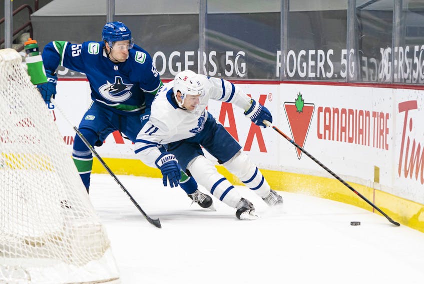 Canucks' Guillaume Brisebois tries to check Maple Leafs' Zach Hyman off the puck at Rogers Arena in Vancouver on Sunday, April 18, 2021. 