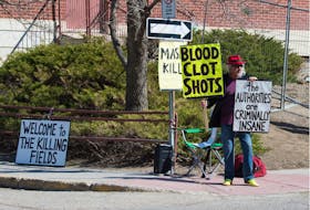 An anti-vax demonstrator holding signs containing misinformation and conspiracy theory slogans stands outside the Regina General Hospital on April 21, 2021.
