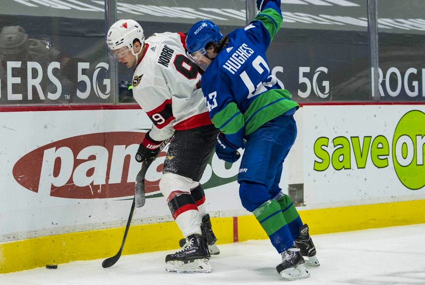 Senators centre Josh Norris (9) protects the puck during a battle along the boards with Canucks defenceman Quinn Hughes in the second period of Thursday's game at Rogers Arena in Vancouver.