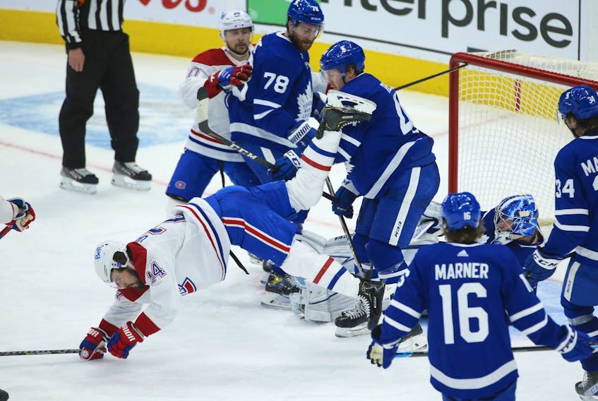 Montreal Canadiens' Phillip Danault is flattened by Maple Leafs' Morgan Rielly after slamming into goalie Jack Campbell during a scramble in front of the net during the third period in Toronto on Wednesday, April 7, 2021.