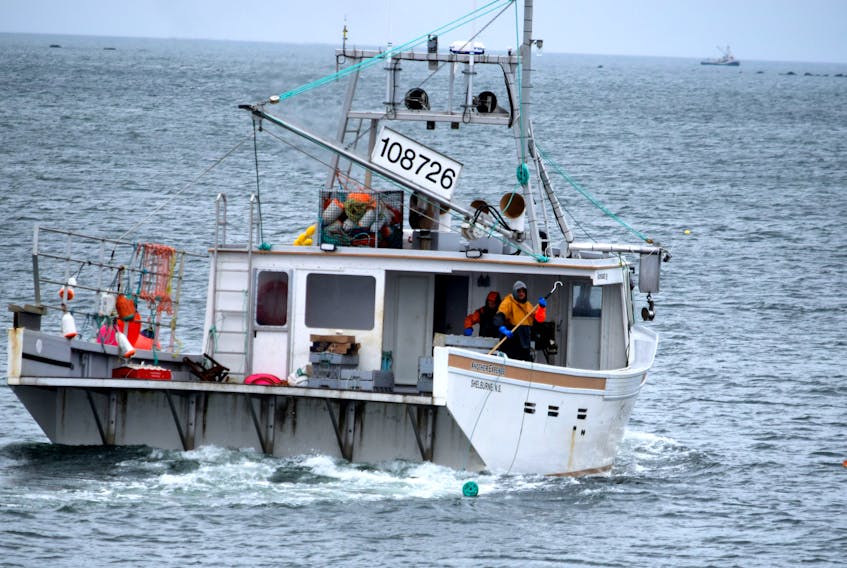 One crewman stands at the ready with a gaff to grab the approaching buoy line in the water while the other tends to the catch  aboard the fishing vessel Another Expense while fishing lobster along the Woods Harbour coastline. The six-month commercial lobster  fishery is southwestern Nova Scotia and the South Shore closes on May 31. KATHY JOHNSON
