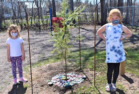 Students Audrey and Avery Johnson stand beside a tree planted on the Debert Elementary School grounds in memory of Lisa McCully who was a victim of last year’s shooting rampage which started in Portapique.