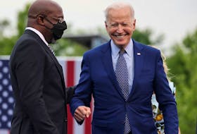 U.S. President Joe Biden smiles next to Senator Raphael Warnock (D-GA) during the Democratic National Committee's "Back on Track" drive-in car rally to celebrate the president's 100th day in office.
