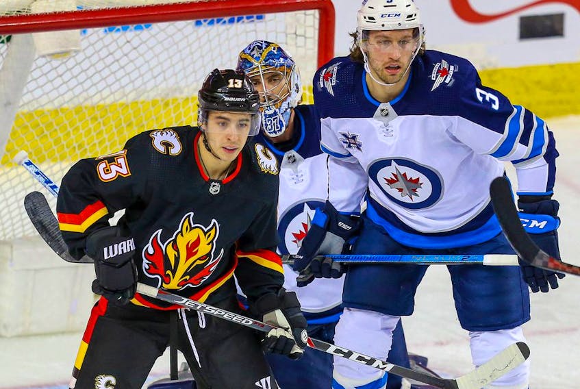 The Calgary Flames’ Johnny Gaudreau and Winnipeg Jets’ Tucker Poolman fight for position in front of Jets goaltender Connor Hellebuyck at the Saddledome in Calgary on Friday, March 26, 2021. 