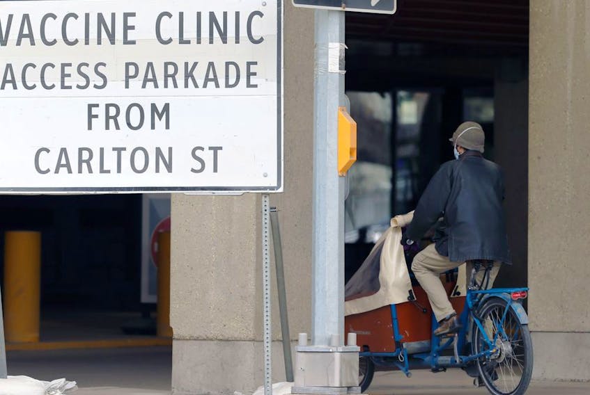 A person cycles by a sign at the COVID-19 vaccination supersite at RBC Convention Centre in Winnipeg on Tuesday, May 4, 2021. 