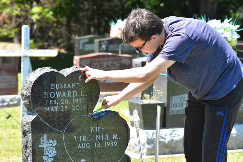 Caelan DeViller uses a toothbrush to clean the smaller nooks and crannies of his grandfather Howard DeViller's gravestone while cleaning it in a Wedgeport, Yarmouth County, cemetery. TINA COMEAU • TRICOUNTY VANGUARD 