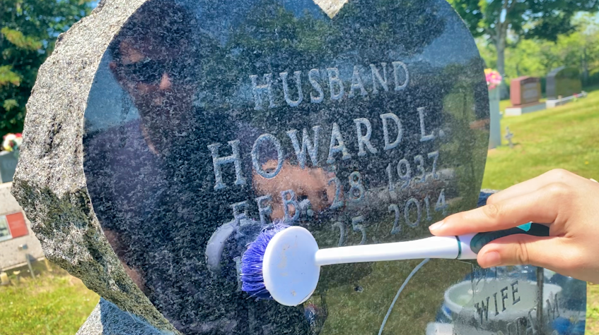 Caelan DeViller's image is reflected on the surface of his grandfather Howard DeViller's gravestone as he cleans it. TINA COMEAU • TRICOUNTY VANGUARD
