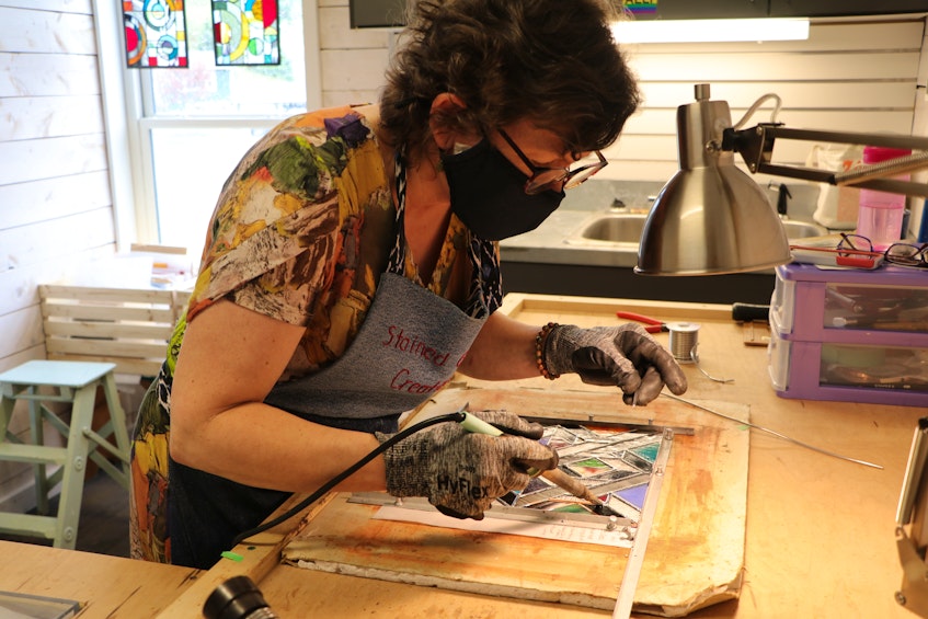Jennifer Walsh, who owns Stained Glass Creations in the Quidi Vidi Village Plantation, works on a stained-glass free-hanging panel Friday. She said she’s anxious to see tourists come through the building again. — Glen Whiffen/The Telegram
