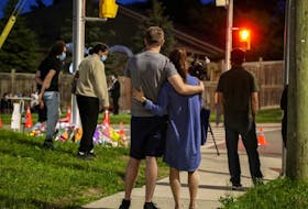 People and members of the media are seen Monday evening at a makeshift memorial at the fatal crime scene where the driver of a pickup truck jumped the curb and ran over a Muslim family in what police say was a deliberately targeted anti-Islamic hate crime, in London, Ont.