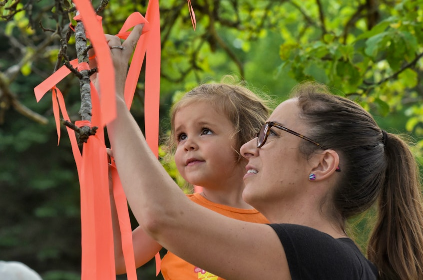 Lisa D'Eon ties an orange ribbon onto a tree in Tusket while her daughter Ada looks on. They were among the participants in a Canada Day morning family walk to honour the children of residential schools. The family walk was seen as a time for reflection and to spread a message of healing. TINA COMEAU • TRICOUNTY VANGUARD 