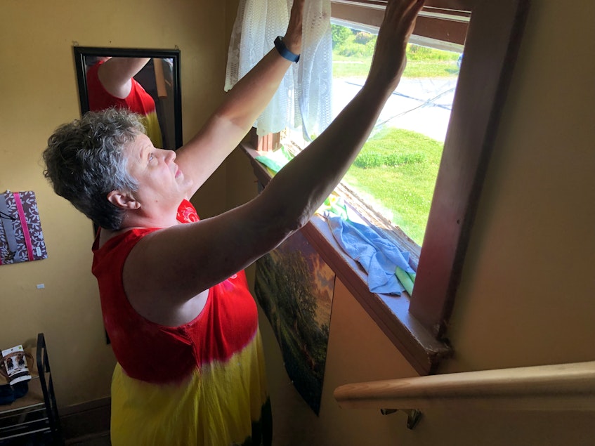 Susan MacNeil, 61, rolls up the curtain on a small window on the main level of her Glace Bay home. On the sill are rolled up cloths and towels, which see keeps there to soak up rain that leaks through. NICOLE SULLIVAN/CAPE BRETON POST