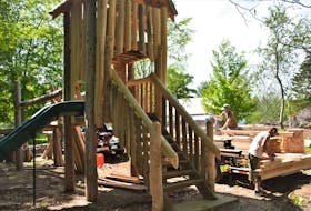 The Log Run, which includes a slide and obstacle course, is part of the playground work being done just outside the Portapique Community Hall. To the side, Andrew MacDonald (on saw) and project co-ordinator Bjorn Merzbach prepare lumber to build play   huts.