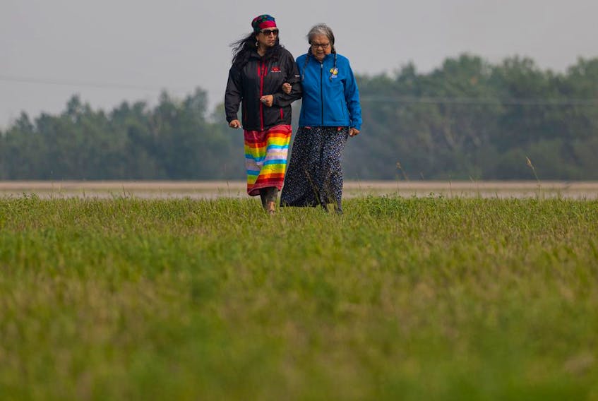  Residential school survivor Senator Jenny Spyglass (right) walks across the field where the search for unmarked graves from children at the Delmas Indian Residential school begins. Photo taken in Delmas, Sask. on Saturday, July 17, 2021.