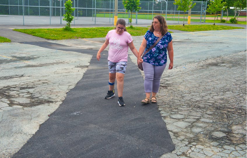 Mairin Lawlor, 12, and her mom Amanda walk on a recently paved strip of parking lot outside Caledonia Junior High on Monday, July 19, 2021. The parking lot is in bad shape, making it difficult for Mairin, who has mobility issues, to get to school. - Ryan Taplin