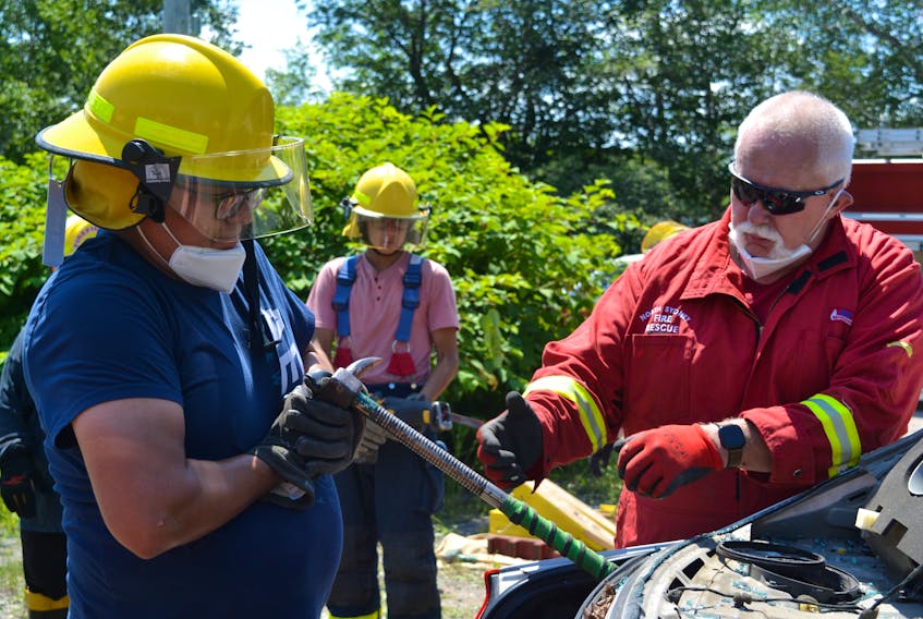 Chris Simon, left,  a volunteer firefighter with We'koqma'q First Nation, pries open the trunk of a car as part of a two day vehicle extrication course, as the instructor,  North Sydney Fire Chief Lloyd MacIntosh, looks on. ARDELLE REYNOLDS/CAPE BRETON POST