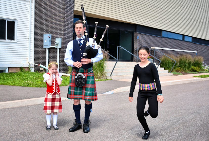 Briar MacHattie covers her ears for protection from the loud drones of the Scottish bagpipe played by her father James, as Emily Austin tap dances to each note outside the College of Piping and Celtic Performing Arts Centre. - Desiree Anstey