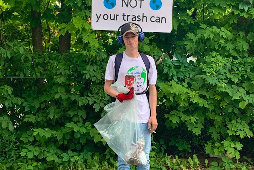 Justin Greeno standing next to his poster with his favourite saying, ‘The World is NOT Your Trash Can.’ Contributed