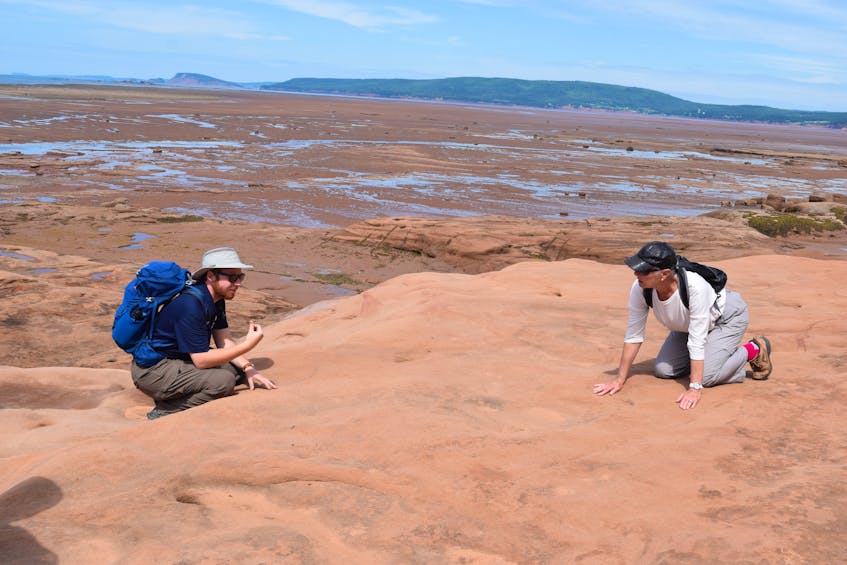 Geoscientist Caleb Grant and participant Rosemary Rowntree kneel down to touch the sand on a surface that appears to be firm and smooth. A large portion of the Thomas Cove walk traverses the wide sandstone ledge. 