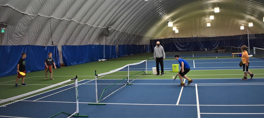 Using a temporary court marked by tape, summer camp attendees Carson Jones (left), Noah Carson, Ferris Rau and Noah Pollard try their hand at pickleball as Cougar Dome manager François Giguere looks on and provides a few pointers. - Richard MacKenzie