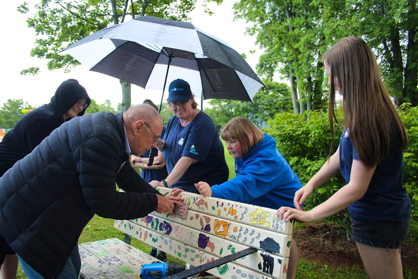 Summerside Girl Guides and Rangers watch Peter Holman, co-chair of the Age Friendly Cities Committee, install a plaque on a bench in Leger Park. - Kristin Gardiner