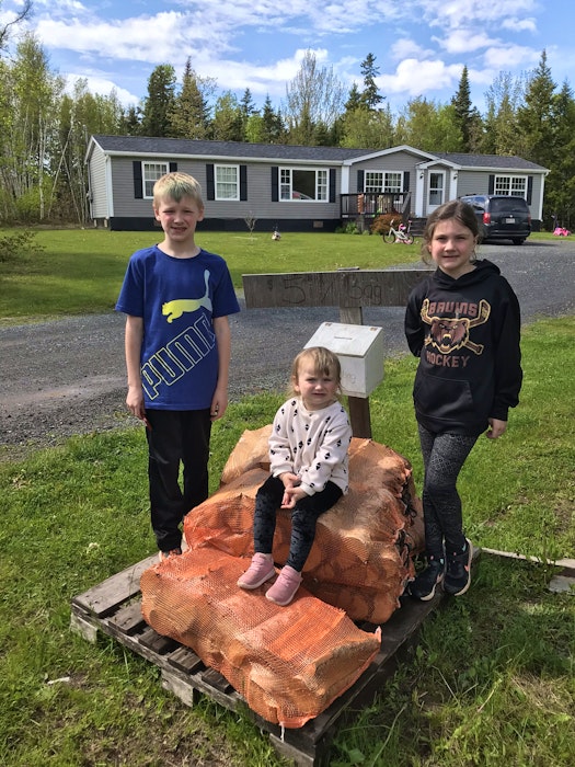 Chermaine Regular's children, from left, Bentley, Allie-Mae and Lilah, stand beside (and sit on) the bundles of firewood they prepare to sell to people visiting the campgrounds near their home in Murray Harbour. Some of the wood was recently stolen, leading to an overwhelming public response in support of the kids.  - Contributed