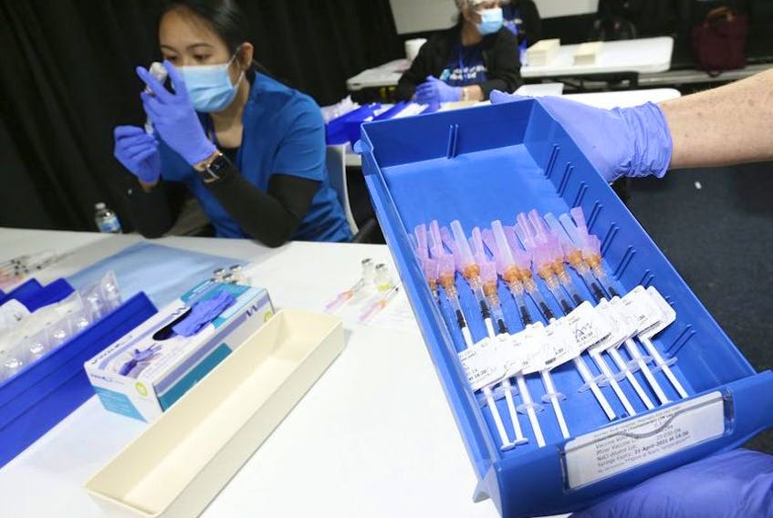 Helen Briggs, a pharmacist, holds up a tray of syringes as Lirie Palamind an RPN  (background) loads up them up with Pfizer-BioNTech COVID-19 vaccine at the Humber River Hospital clinic held at Downsview Arena on April 21, 2021.  