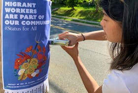 A member of No one is illegal — Halifax/Kjipuktuk puts up a poster which reads: “Migrant workers are part of our community.”