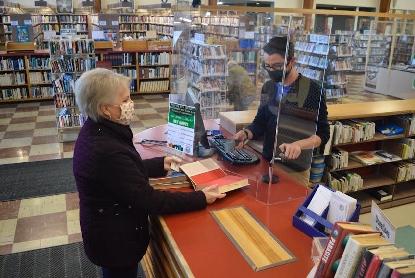 Cape Breton Regional Library patron Rose Mombourquette, left, borrows some books with the help of McConnell library staff member Jonathan Manley who checks them out from behind a partition. DAVID JALA/CAPE BRETON POST